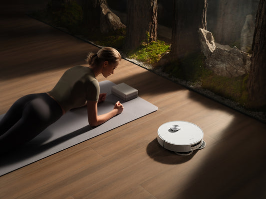 Woman planks on mat near robot vacuum cleaner.